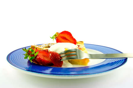 Slice of apple and strawberry pie with strawberries, cream and a fork on a blue plate with a white backgroundの写真素材