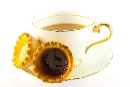 Tea in a cup and saucer with yellow and red jam tarts on a white backgroundの写真素材