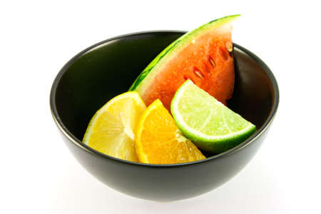 Wedges of lemon, lime and orange in a small black dish with a slice of juicy watermelon on a white backgroundの写真素材