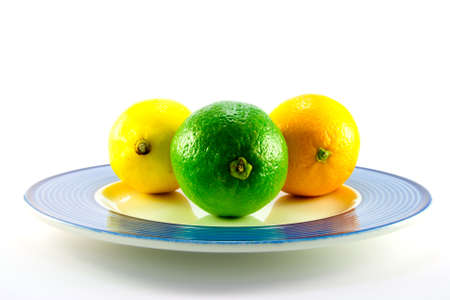 Single whole lemon, lime and orange on a blue plate with a white backgroundの写真素材