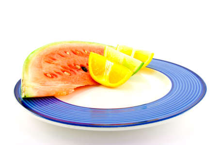 Slice of juicy red watermelon with lemon, lime and orange wedges on a blue plate with a white backgroundの写真素材