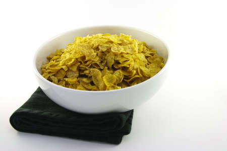 Golden crisp cornflakes in a round white bowl with a black napkin on a white background