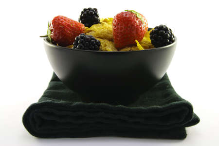 Cornflakes with strawberries and blackberries in a round black bowl with a black napkin on a white backgroundの写真素材