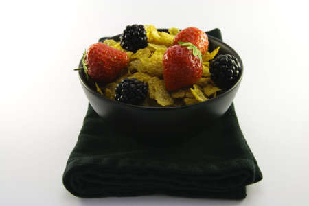 Cornflakes with strawberries and blackberries in a round black bowl with a black napkin on a white backgroundの写真素材
