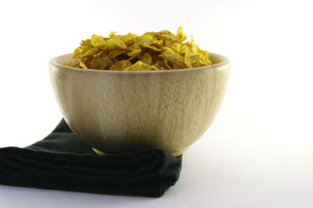 Golden crisp cornflakes in a round wooden bowl with a black napkin on a white background