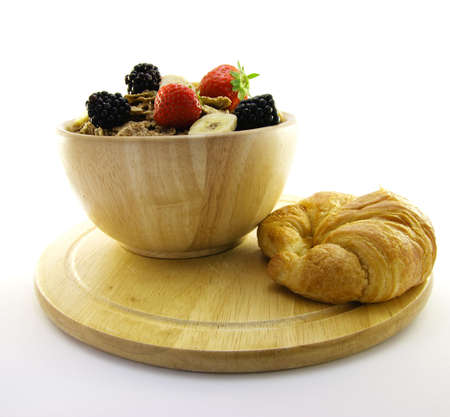 Crunchy looking delicious bran flakes and juicy fruit in a wooden bowl with a croissant on a white backgroundの写真素材