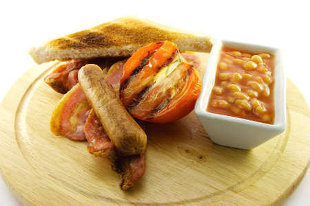 Delicious cooked breakfast items and baked beans on a wooden plate on a white backgroundの写真素材