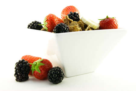 Crunchy delicious looking bran flakes and juicy fruit in a white bowl on a white background