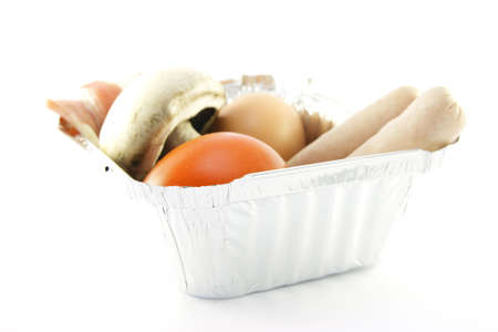 Uncooked sausage, bacon, mushroom, egg and tomato on a round plate with a white backgroundの写真素材