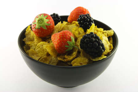 Cornflakes with strawberries and blackberries in a round black bowl on a white backgroundの写真素材