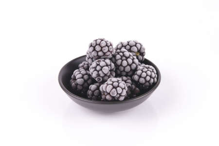 Black ripe frozen blackberries in a small round black dish with a reflective white backgroundの写真素材
