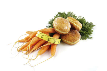 Contradiction between healthy food and junk food using bunch of carrots and doughnut with a tape measure on a reflective white background の写真素材