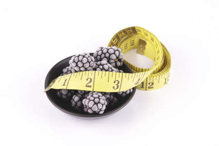 Black ripe frozen blackberries in a small round black dish with a tape measure on a reflective white backgroundの写真素材