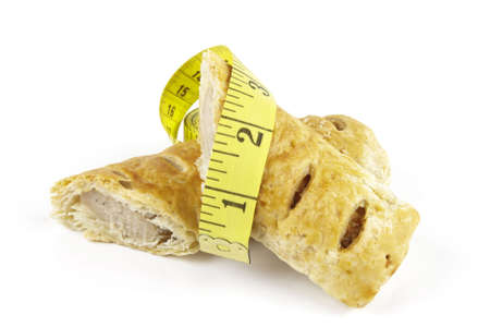 Single golden sausage roll cut in half with yellow tape measure on a reflective white backgroundの写真素材