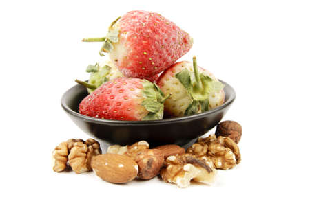 Red ripe frozen strawberries in a small black bowl with mixed nuts on a reflective white backgroundの写真素材