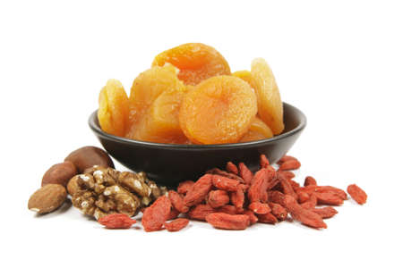 Dried juicy orange apricots with mixed nuts and goji berries in a small black bowl on a reflective white backgroundの写真素材