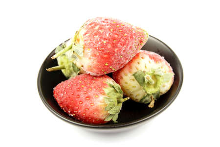 Red ripe frozen strawberries in a small black bowl on a reflective white backgroundの写真素材