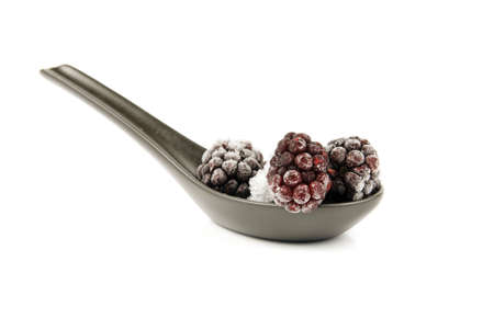 Ripe frozen blackberries on a small black spoon with a reflective white backgroundの写真素材