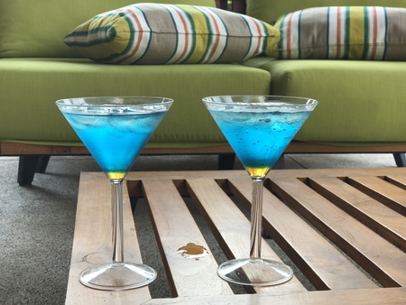 Blue and yellow cocktails in martini glasses on coffee table and green sofa with strippes cushionの写真素材