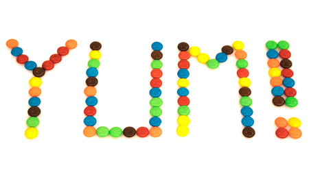 Yum word written with colorful button shaped chocolates candy isolated on white backgroundの写真素材