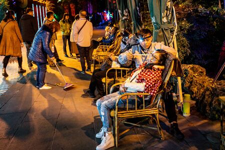 22 november 2017, Chengdu Sichuan China : Chinese girl doing the ear cleaning custom in the Jinli ancient street of Chengdu at night in Sichuan Chinaのeditorial素材
