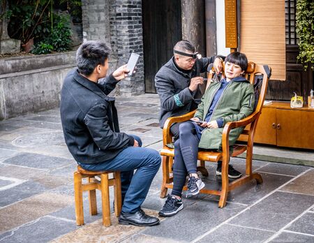 22 november 2017, Chengdu Sichuan China : Chinese woman doing the ear-cleaning in the Wide and Narrow alleys of Chengdu with her boyfriend taking pictures in Chinaのeditorial素材