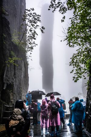 26 April 2018, Enshi Hubei China : Chinese tourists wearing colorful plastic raincoats in front of stone karst pillar called the stick of incense in the clouds of Mufu Grand Canyon in Enshi Chinaのeditorial素材