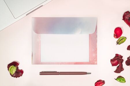 Feminine workspace with blank open letter laptop computer writing supplies and pink dried flowers...