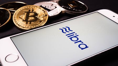 26 June 2019, Wuhan China: Libra the Facebook cryptocurrency logo on mobile phone screen and real coins of other crypto such as Bitcoin next to itのeditorial素材