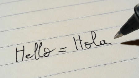 Beginner Spanish language learner writing Hello word Hola for homework on a notebook macro shot