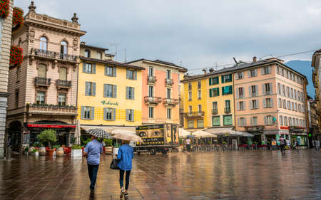 Lugano Switzerland, 1 July 2020: People with umbrellas on rainy overcast day on Piazza della Riforma square with colorful buildings in Lugano Ticino Switzerlandのeditorial素材