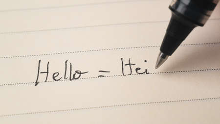 Beginner Finnish or Norwegian language learner writing Hello word Hei for homework on a notebook macro shotの写真素材