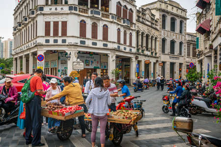 Haikou China, March 21, 2021: Tourists buying fruits at street food stall in Water-alley street with old colonial buildings and people in Haikou old town Hainan Chinaのeditorial素材