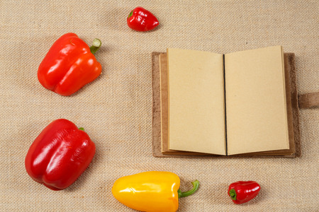 Yellow and Red Pepper with Opened Notebook lying on a sackcloth surface