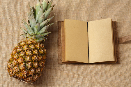 Fresh Ananas and Notebook lying on a sackcloth surfaceの写真素材