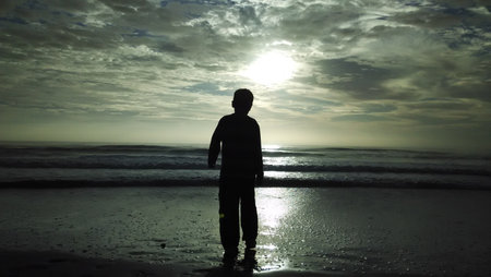 Silhouette of a man standing on the beach at sunset.の写真素材