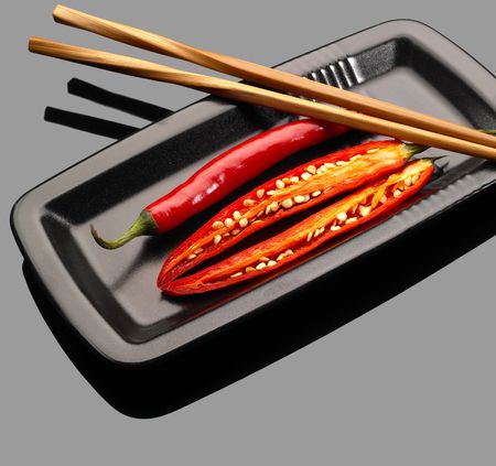 fresh red chili peppers on a plate with chopstikcs over grey reflective surfaceの写真素材