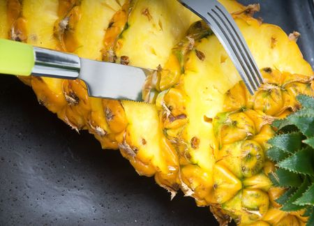 ripe vivid pineapple sliced on a black plate with knife and forkの写真素材