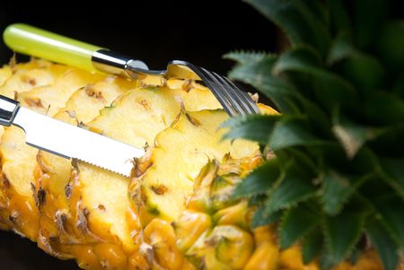 ripe vibrant pineapple sliced on a black plate with knife and forkの写真素材