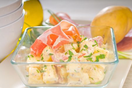 fresh home made parma ham and potato salad,with raw ingredients around with bowls and dishware on a tableの写真素材