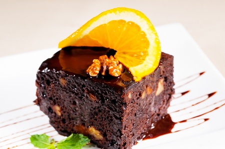 fresh baked delicious chocolate and walnuts cake with slice of orance on top and mint leafの写真素材