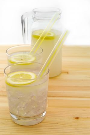 fresh lemonade drink with lemon slice closeup and pitcher carafe over pinewood tableの写真素材