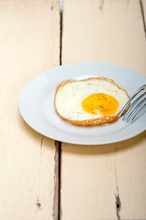 fried egg sunny side up on a plate with fork over wood tableの写真素材