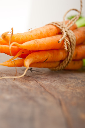 fresh baby carrots bunch tied with rope on a rustic tableの写真素材