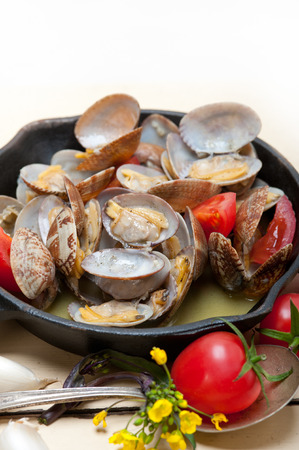 fresh clams stewed on an iron skillet over wite rustic wood tableの写真素材