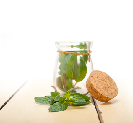 fresh mint leaves on a glass jarover a rustic white wood table