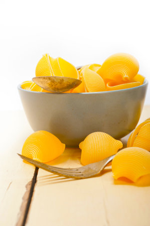 raw Italian snail lumaconi pasta on a blue bowl over rustic table macroの写真素材