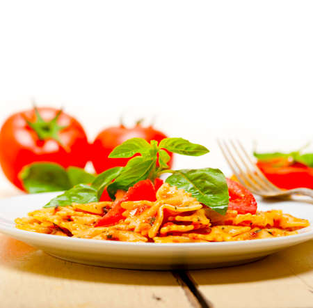 Italian pasta farfalle butterfly bow-tie with tomato basil sauce over white rustic wood tableの写真素材