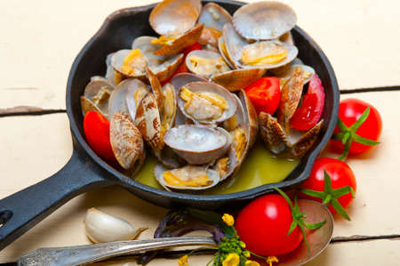 fresh clams stewed on an iron skillet over wite rustic wood tableの写真素材