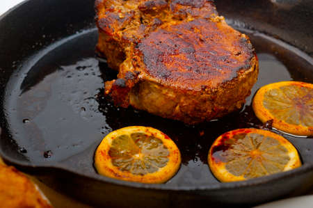 pork chop seared on iron skillet with lemon and spices seasoning
